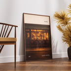 Framed artwork of a pub scene leaning against a wall next to a wooden chair and decorative plants.